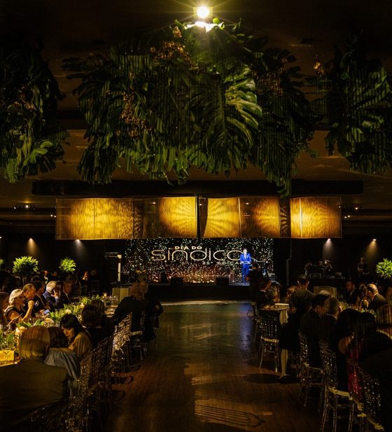 Salão do jantar com mesas decoradas e folhagens no teto, com o palco ao fundo