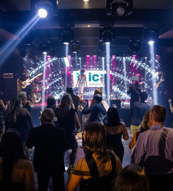 Show da banda no palco com feixes de luz e convidados dançando na frente